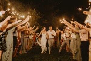 Bride and groom joyfully exit surrounded by sparkling celebratory guests at a nighttime wedding.